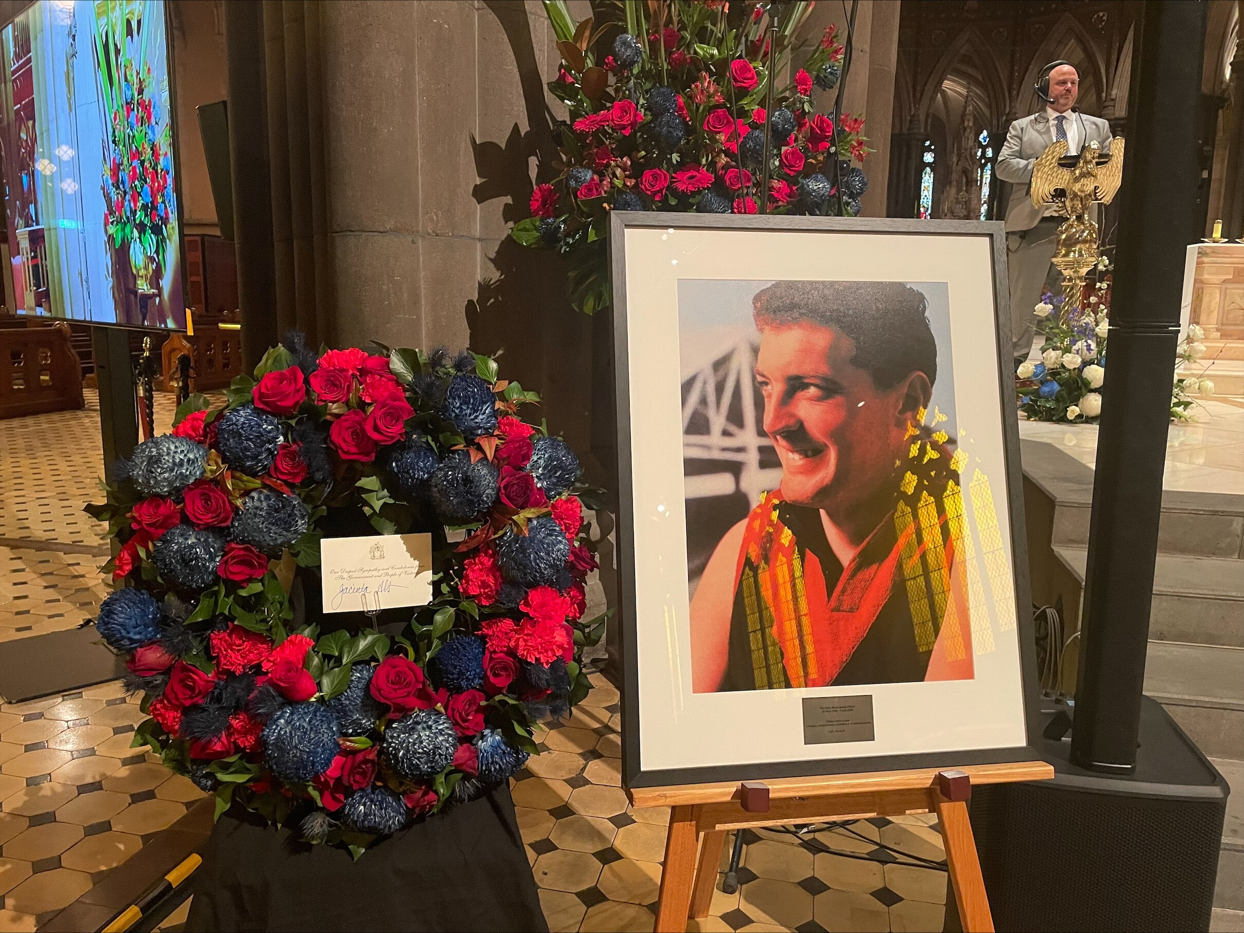 A large picture of the Honourable Brian James Dixon sits next to a rosary of red and dark blue flowers.