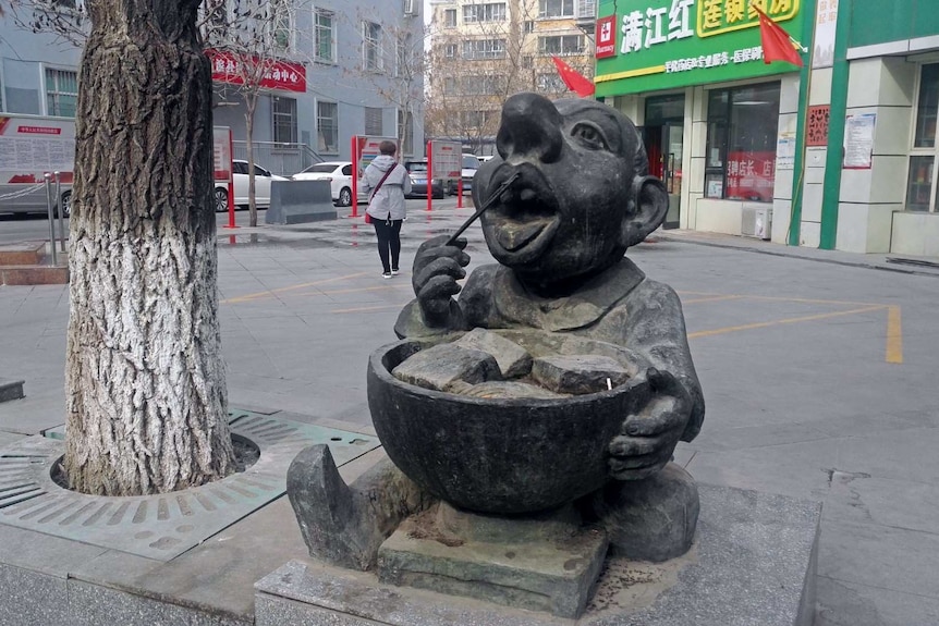 A statue of man eating from a bowl with chopsticks.