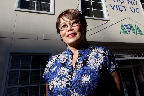 Woman in blue and white blouse standing in front of a building adorned in Vietnamese writing.