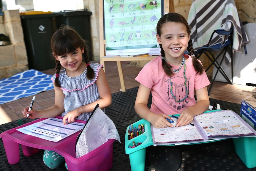 Hallie and Charlotte Williams sitting at colourful outdoor desks, doing their school work.