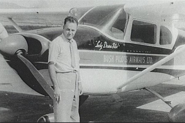 Historic black and white photo of a man standing beside a small plane.