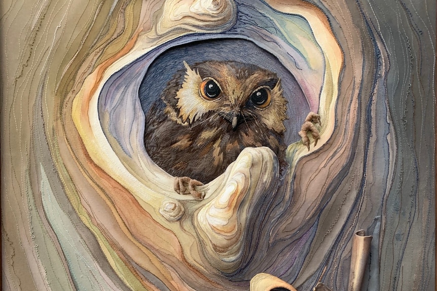 Textile picture with an owl peeking through a tree hollow. 