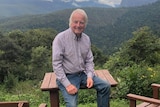 A man sitting on a table smiling with a view of the mountains behind him