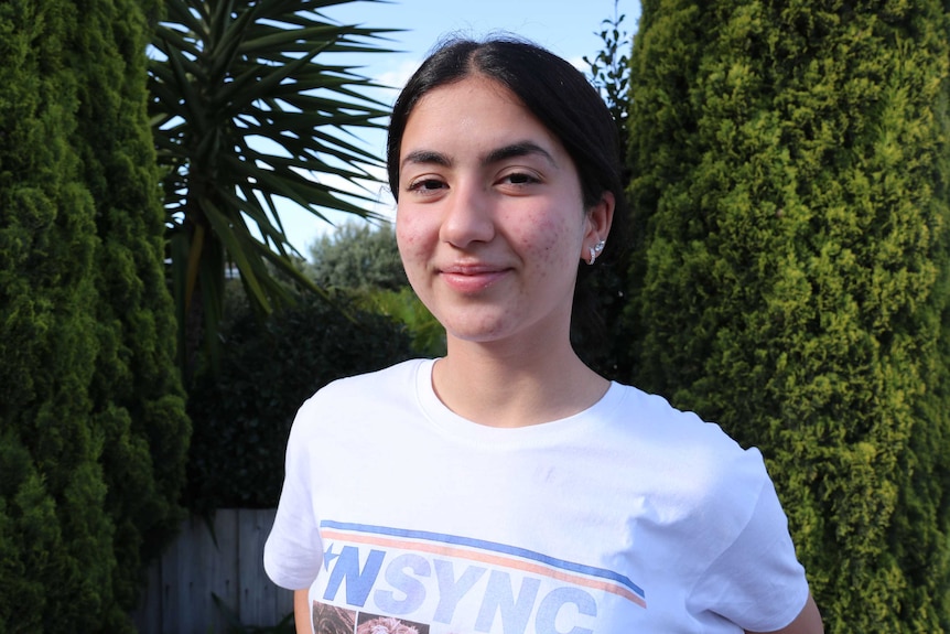 A teenager smiles at the camera in front of some greenery