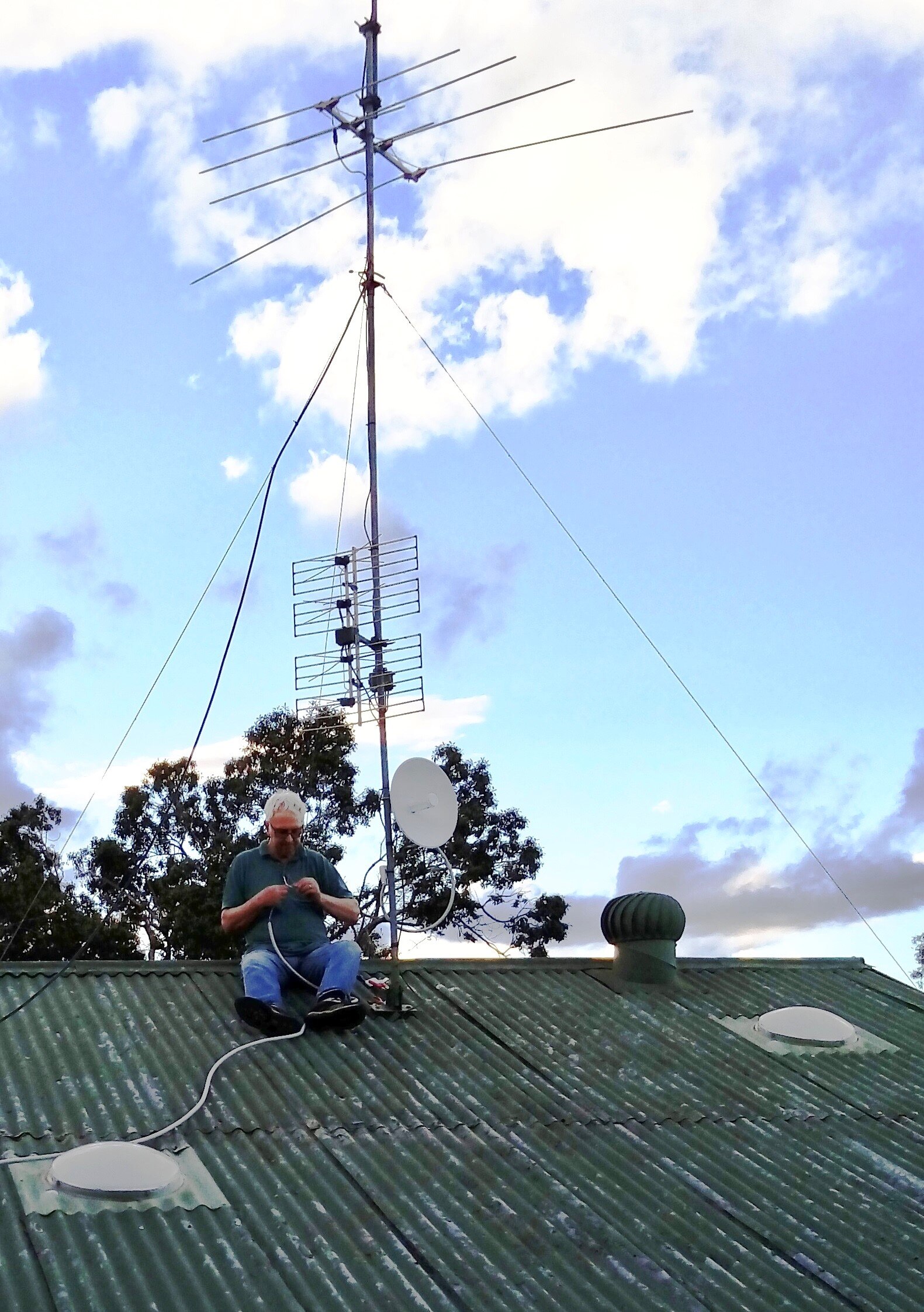 A man works with a piece of wire while sitting on a roof.