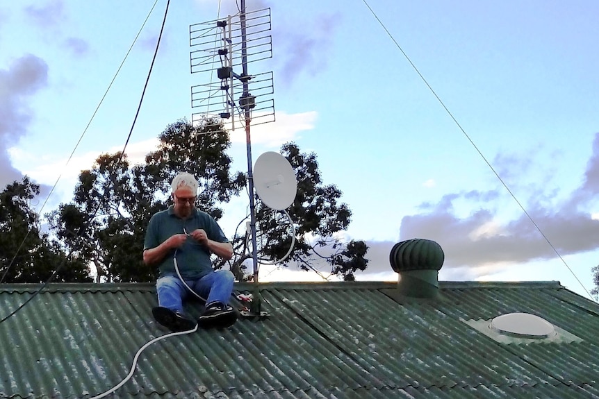 A man works with a piece of wire while sitting on a roof.
