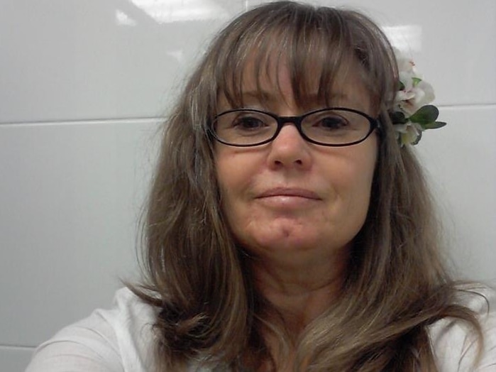 Nicola is wearing a flower in her hair in the selfie taken against a white tiled wall.