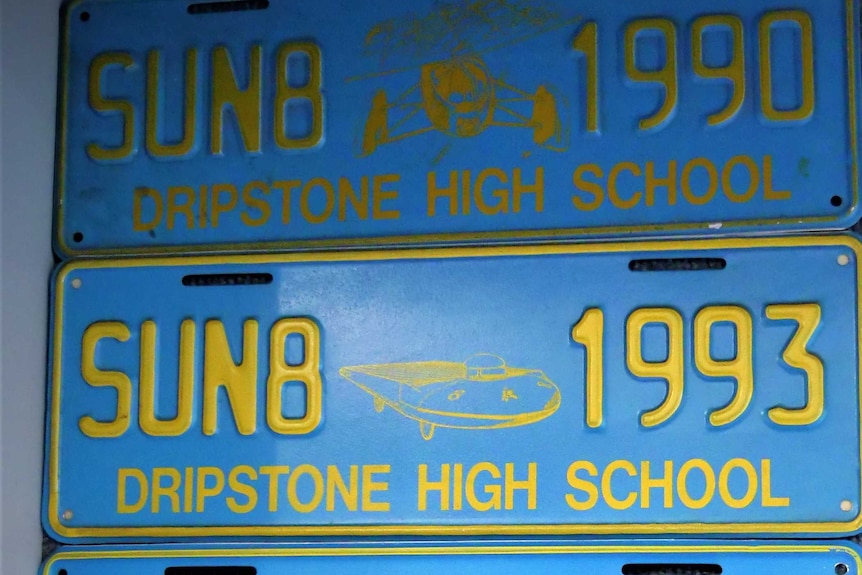 Four blue and yellow numberplates in a display cabinet.