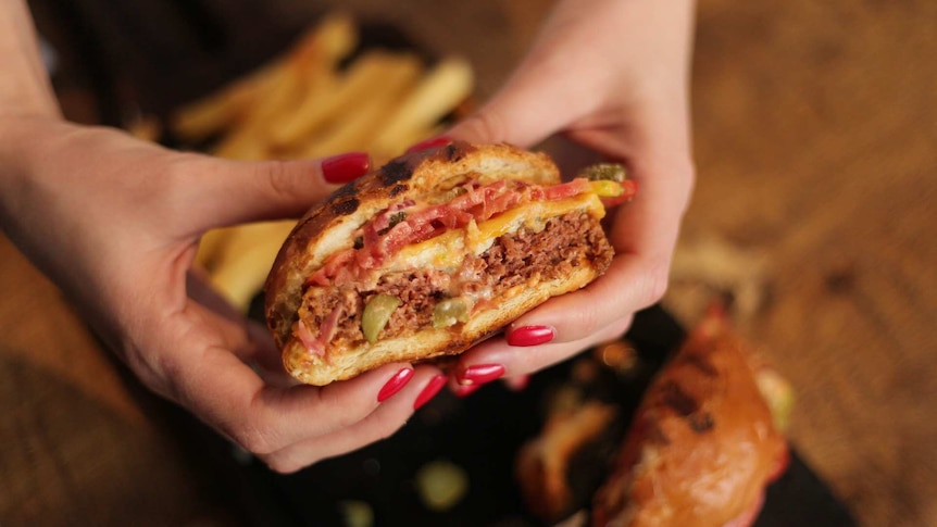 A woman holds up a fake meat burger cut in half, showing a pretty convincing meat patty