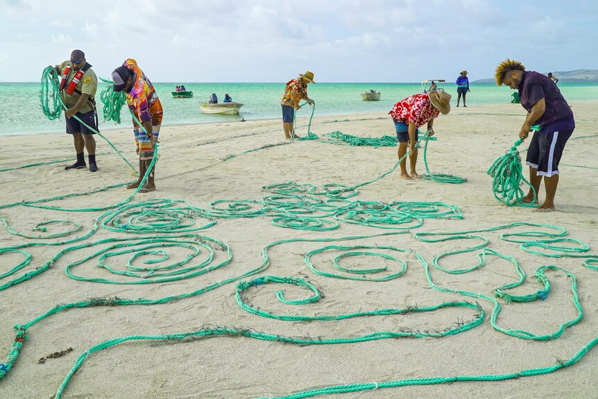 Men rolling up ropes on the beach as the ropes lay stretched out on the sand on Erub (Darnley island) on Torres Strait