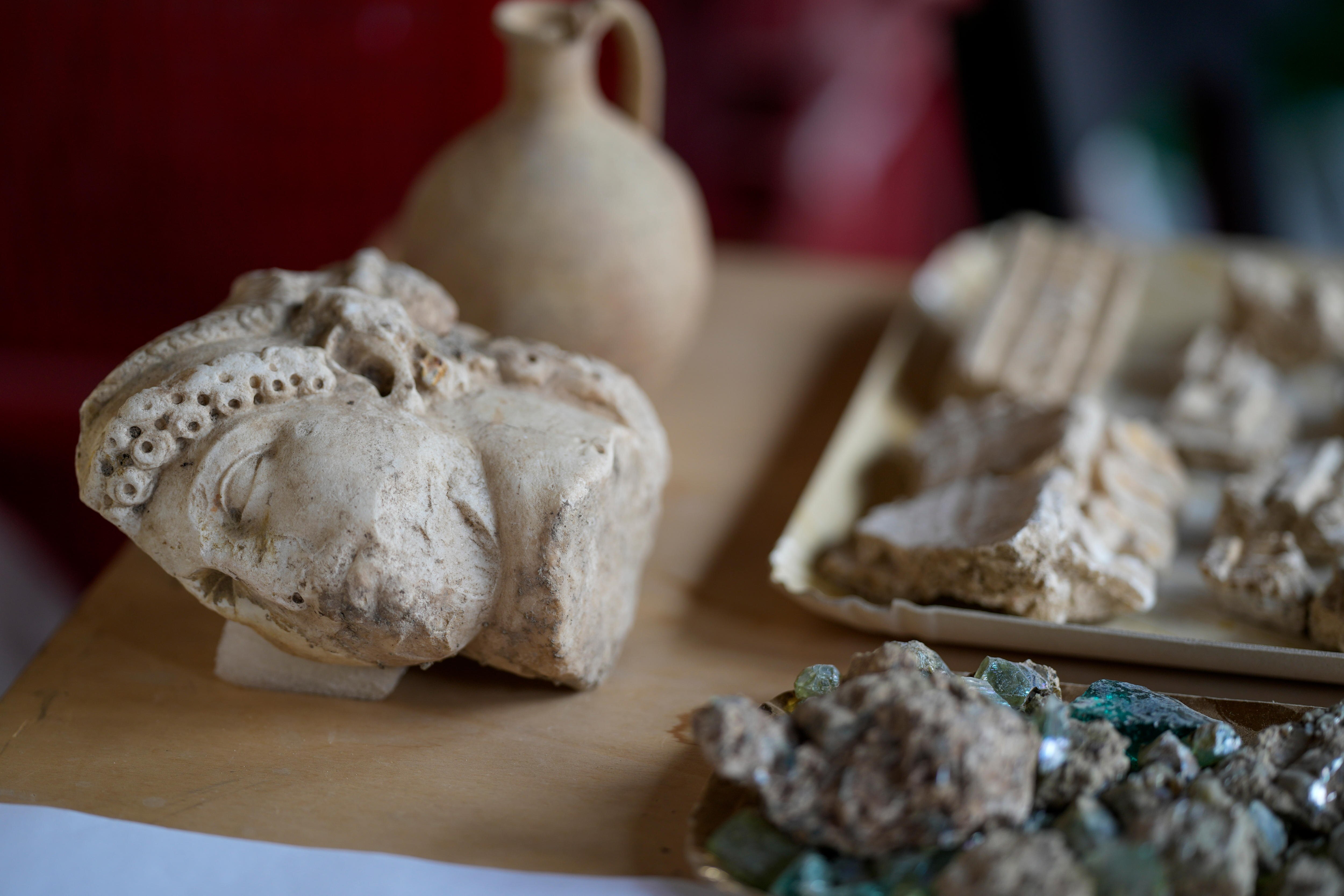 An ancient roman rock artifact in the shape of a face on a table next to other rock ruins