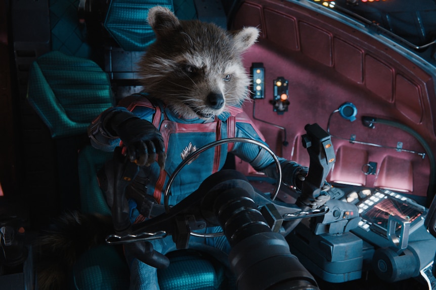 An animated racoon wearing a dark-toned spacesuit behind the wheel of a spacecraft, in a scene from Guardians of the Galaxy 3