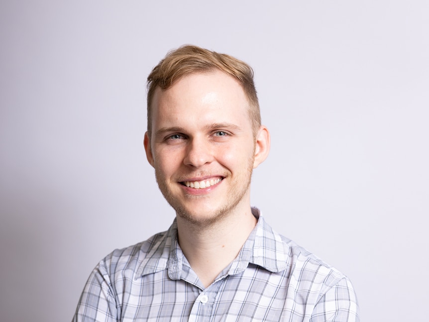 A man with a checkered button up shirt, arms folded and smiling