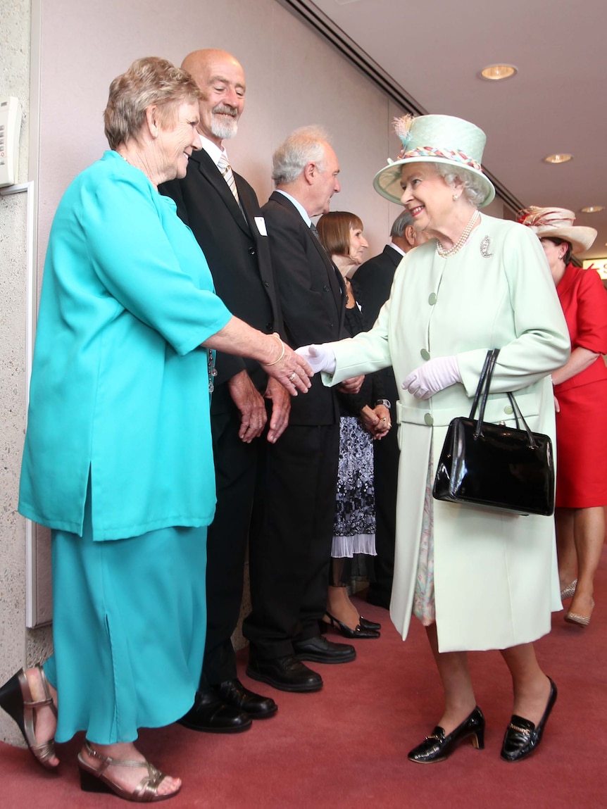 Queen Elizabeth reaches hand to older woman in blue suit