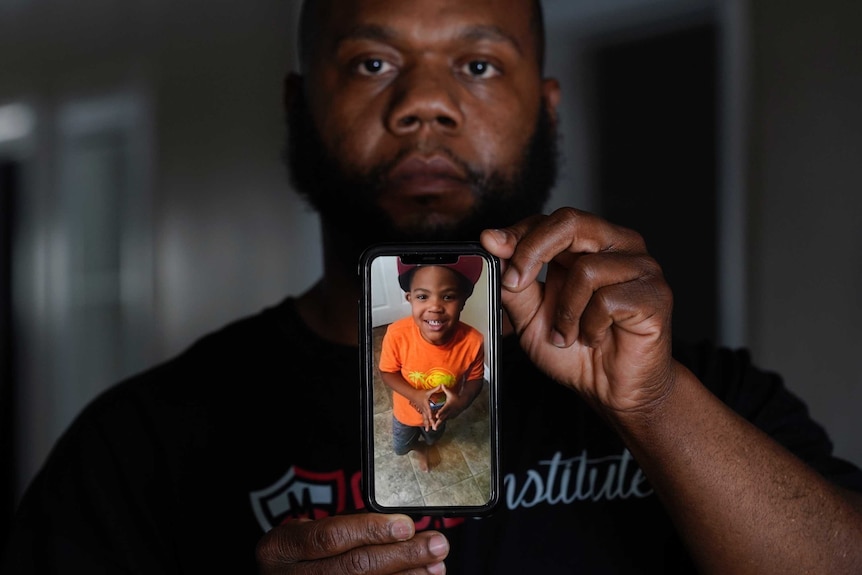A man holds a picture of his son displayed on a mobile phone.