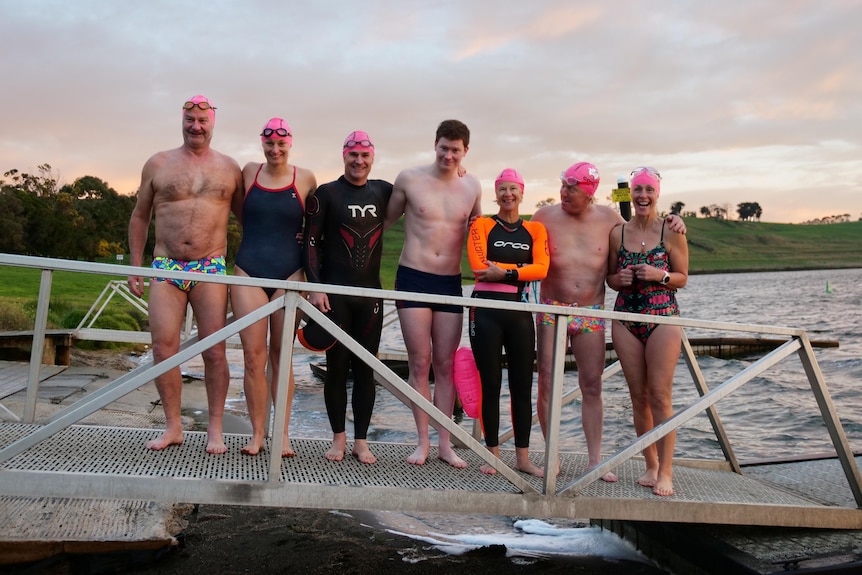 Swimmers in pink caps lined up on a lake ramp for a group photo
