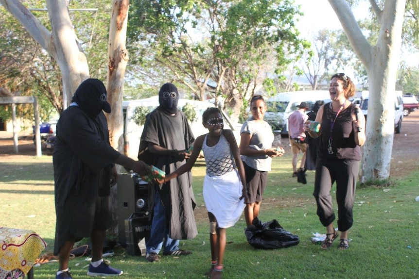 A girl laughs as she takes a wrapped present from two large, black-clad people in bird costume