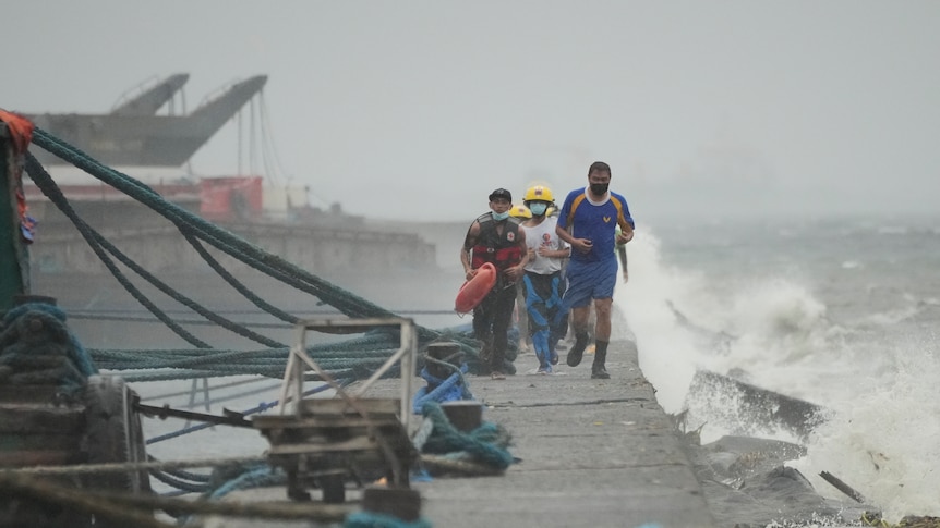 People run down a dock while winds and waves increase in severity. 