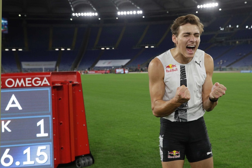 A pole vaulter screams in jubilation with his eyes closed and fists clenched, next to his WR height.