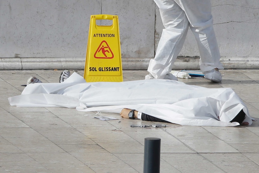 An investigative police officer works by a body under a white sheet after the attack at Marseille's train station.