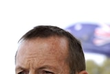 Tony Abbott speaks with the Australian flag in the background