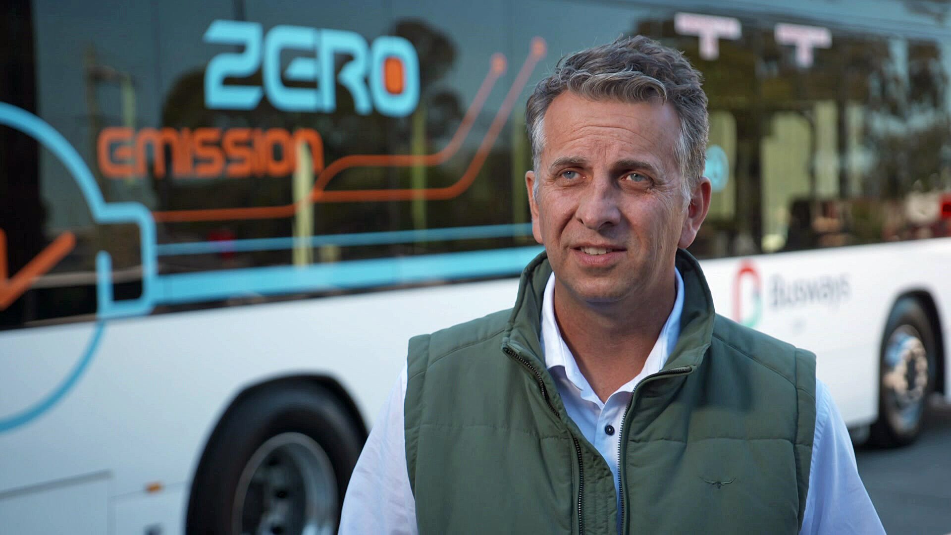 A man wearing a green vest over a blue collared shirt.