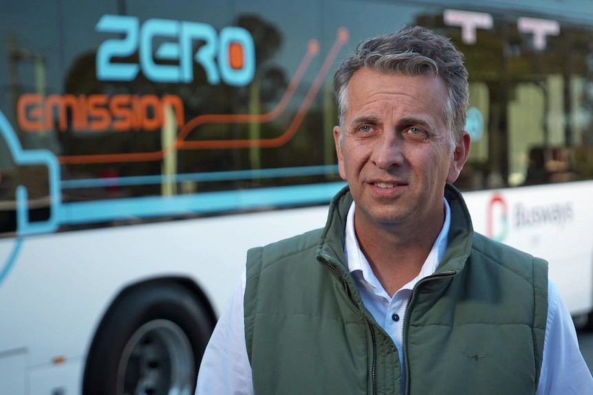 A man wearing a green vest over a blue collared shirt.