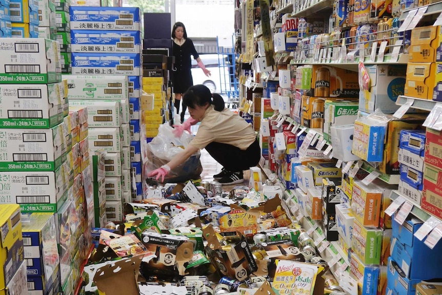 Two shop assistants clean up after an earthquake knocked cans off a supermarket shelf and onto the floor