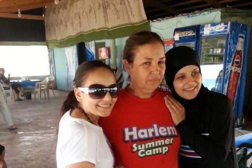 Three women stand side by side hugging and smiling