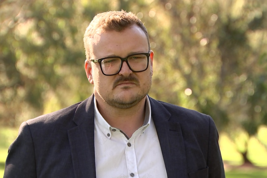 A man wearing glasses standing in a park.