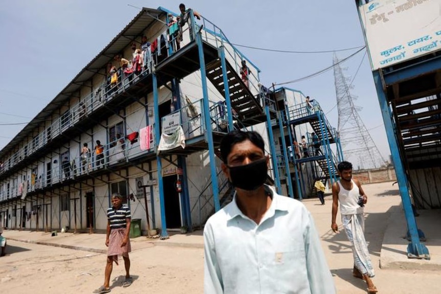 Men wearing face masks stand outside a building in India.
