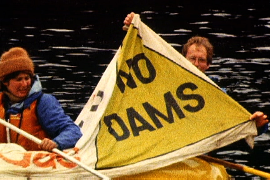 A man in a kayak holds up a yellow sign that says "No Dams"