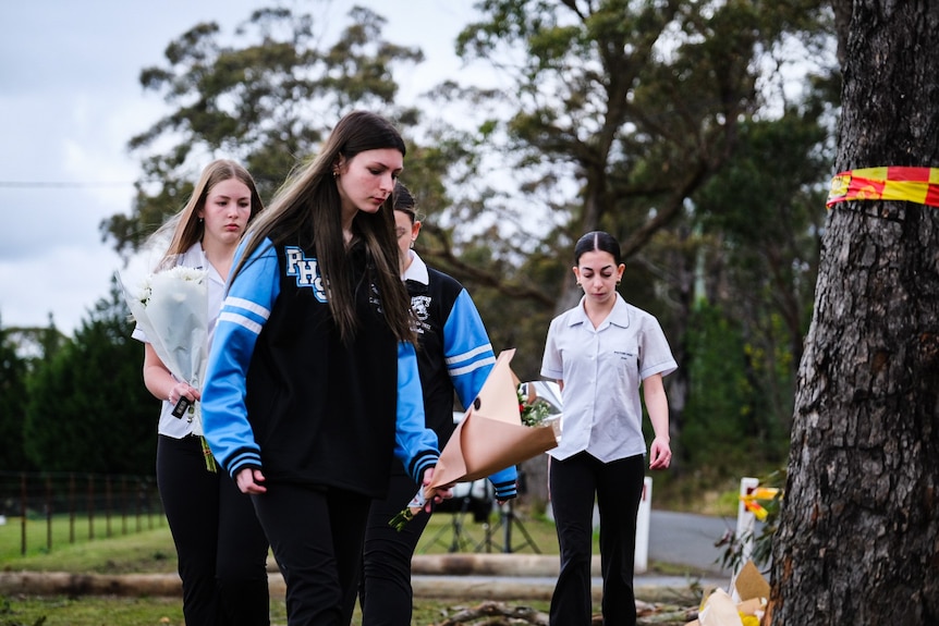 Teenage girls carry flowers to a tree