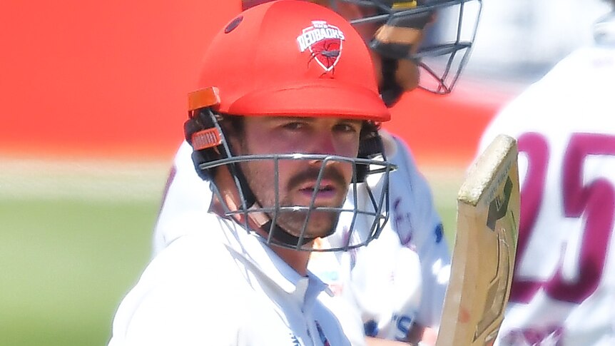 South Australia batter Travis Head raises his bat and looks at the camera during a Sheffield Shield game.