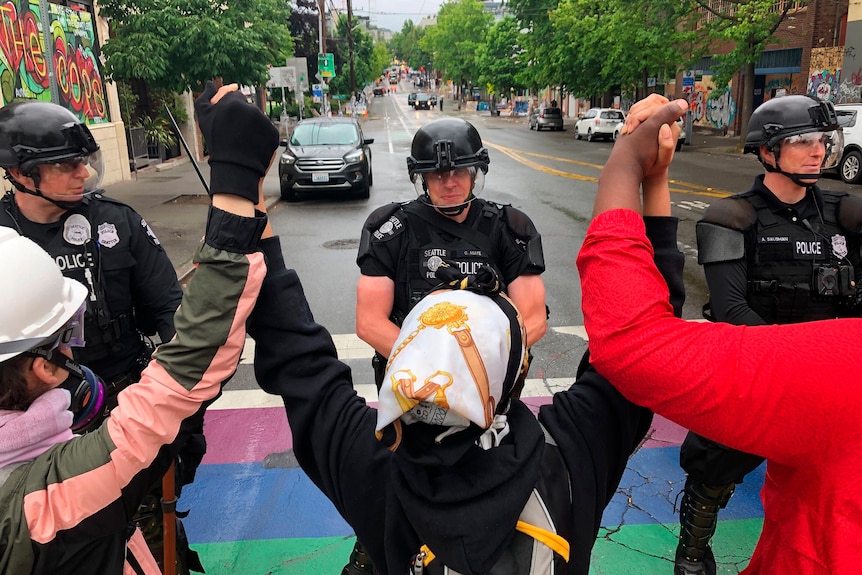 Protesters hold hands in front of a line of police.