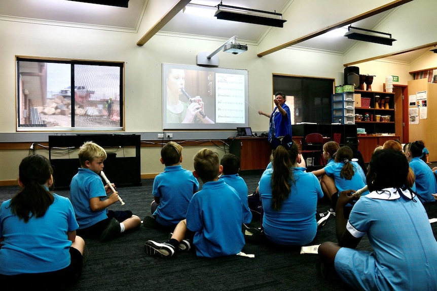 A teacher instructs a group of young primary school aged children how to play recorders in a classroom.