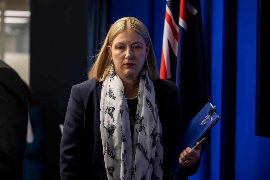 A woman walks inot a room holding a folder 