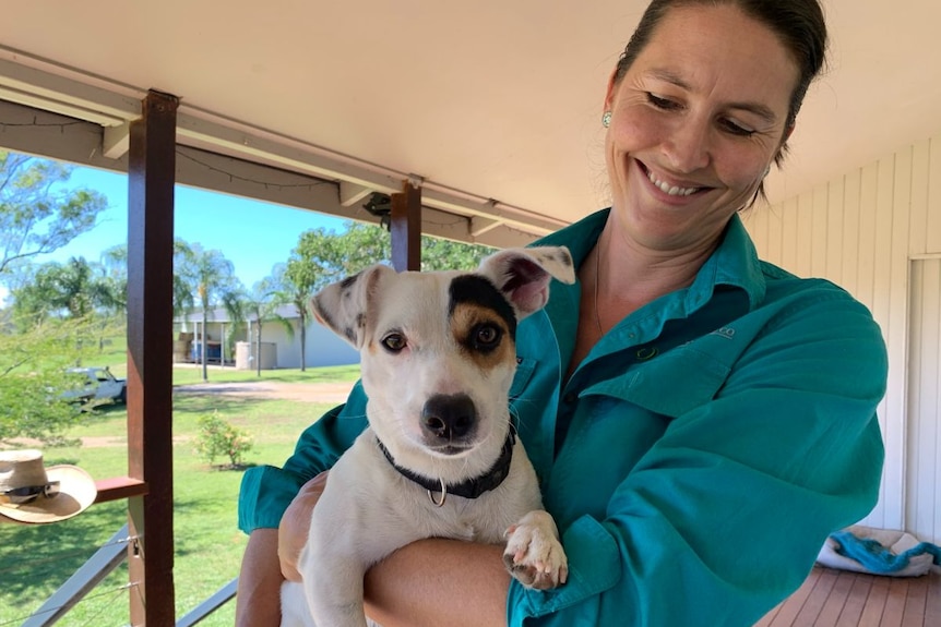 A woman in a blue shirt holds a jack russel in her arms and smiles.