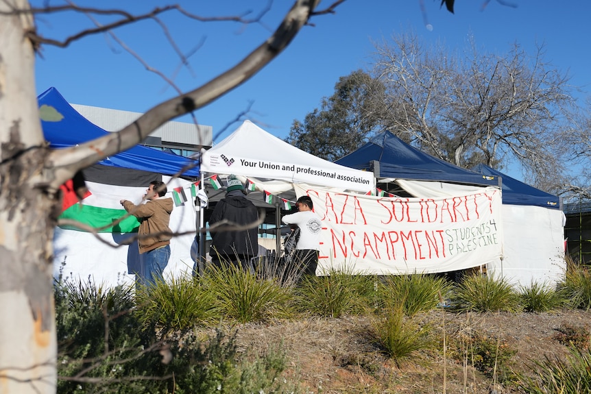 Students stringing up a sign that says "Gaza solidarity encampment" across a tent.