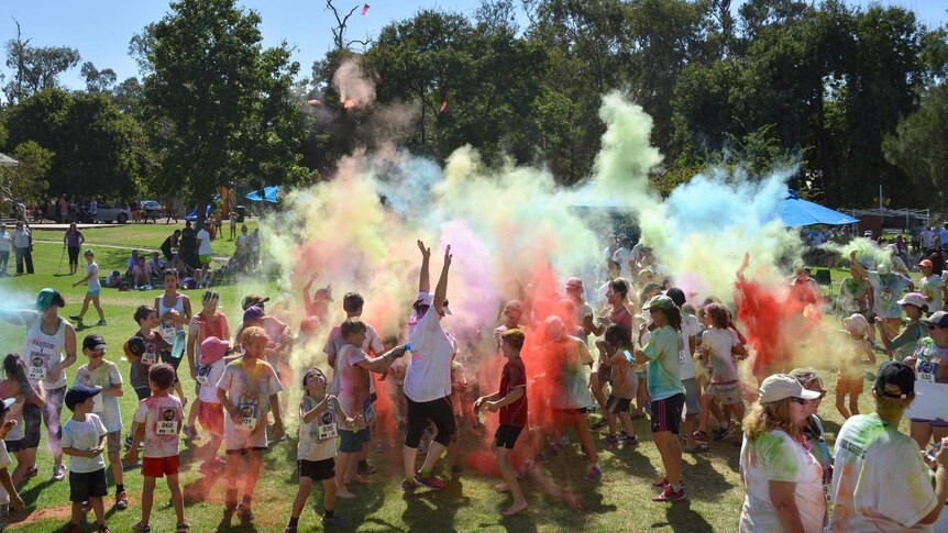 A could of coloured powder fills the air around dozens of people, coloured by the same powder, in a park.