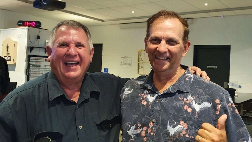 Neil Fisher and Tony Williams smiling, both wearing button up shirts, clock behind say 11:42.