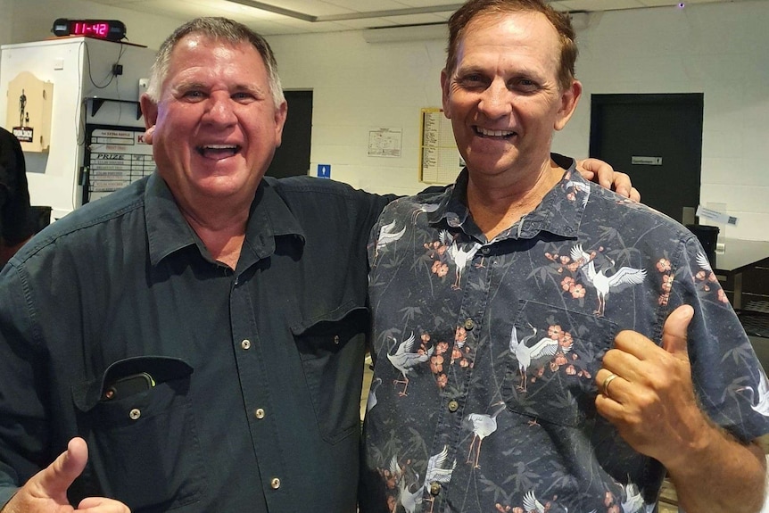 Neil Fisher and Tony Williams smiling, both wearing button up shirts, clock behind say 11:42.