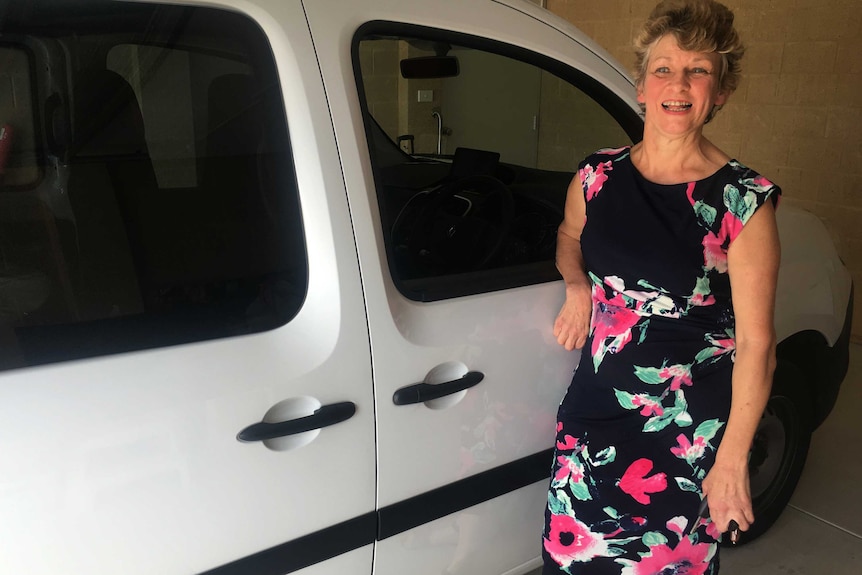 A woman stands next to a white van in a garage.