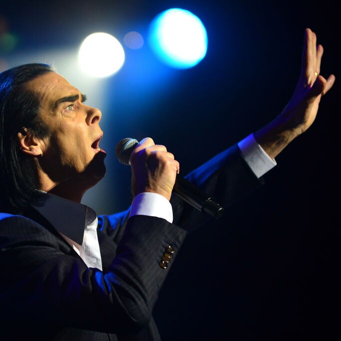 Nick Cave singing passionately with his arm upstretched to the sky.