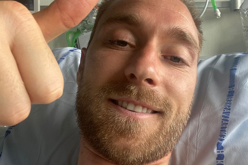Denmark midfielder Christian Eriksen lies in a hospital bed smiling and giving a thumbs-up. 