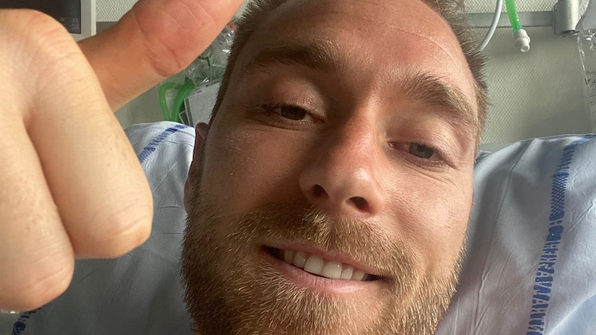 Denmark midfielder Christian Eriksen lies in a hospital bed smiling and giving a thumbs-up. 