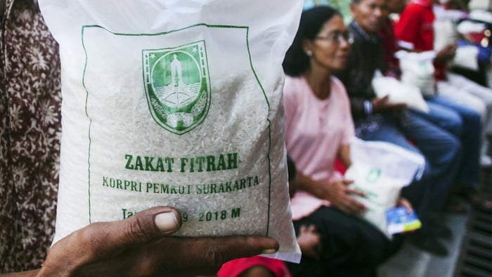 A close-up photo of a hand holding a plastic bag of rice weighing approximately 2kg with residents in the background.