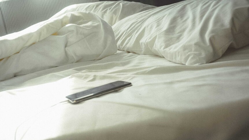 A phone sits on an unmade bed