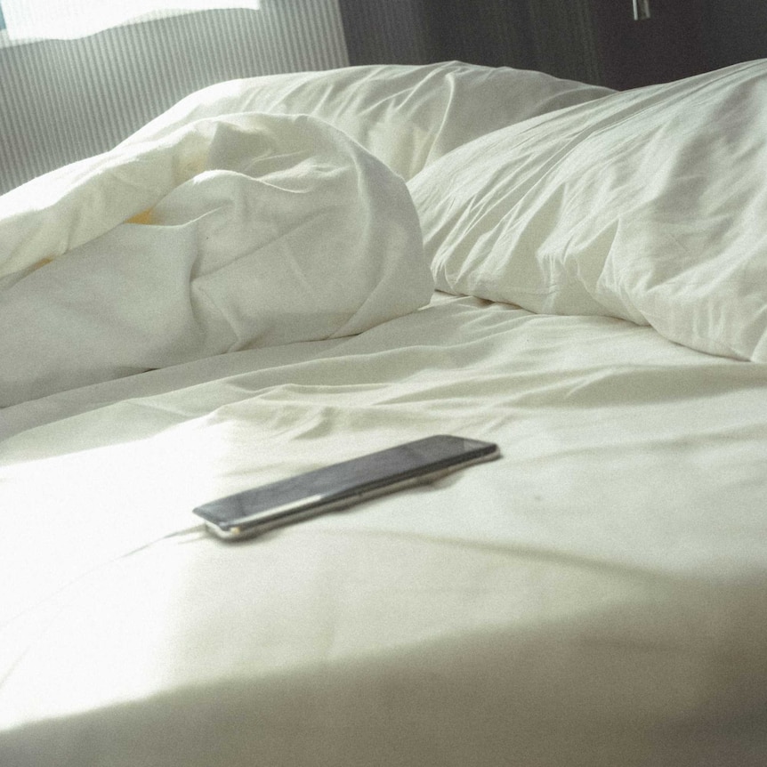 A phone sits on an unmade bed