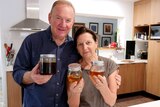 Graeme Connors with his wife Lyn, holding jars of honey and smiling to the camera.